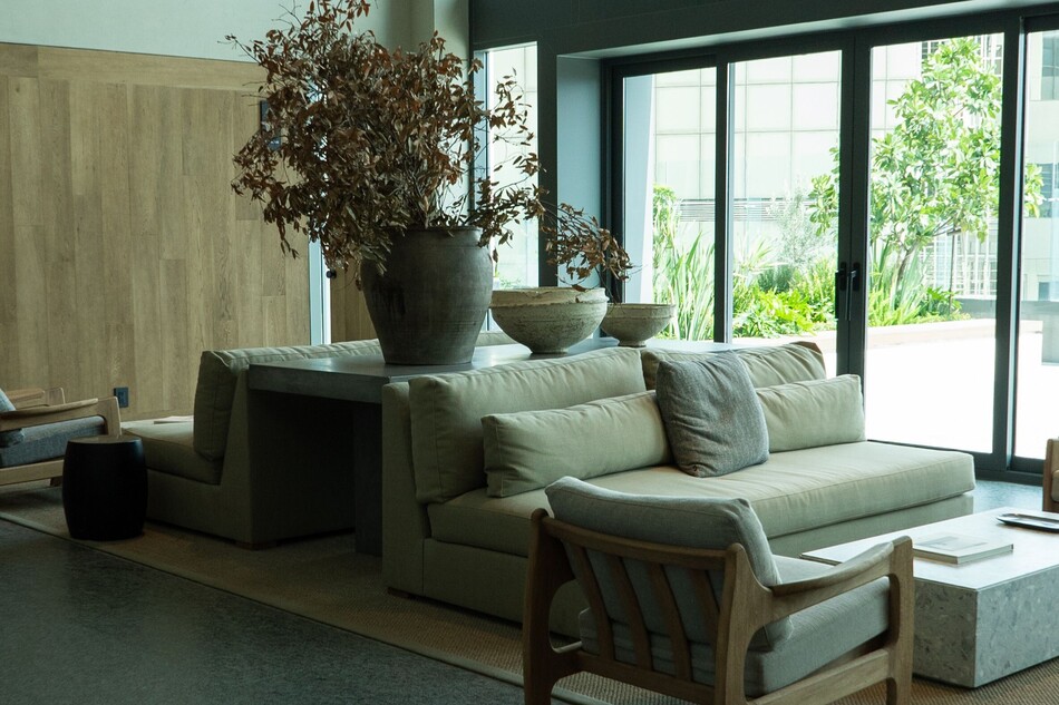Salón de diseño en una vivienda premium decorado bajo el concepto de lujo silencioso, con sofás de tonos neutros, un gran jarrón de cerámica artesanal con ramas secas y grandes ventanales con vistas a una terraza exterior ajardinada.